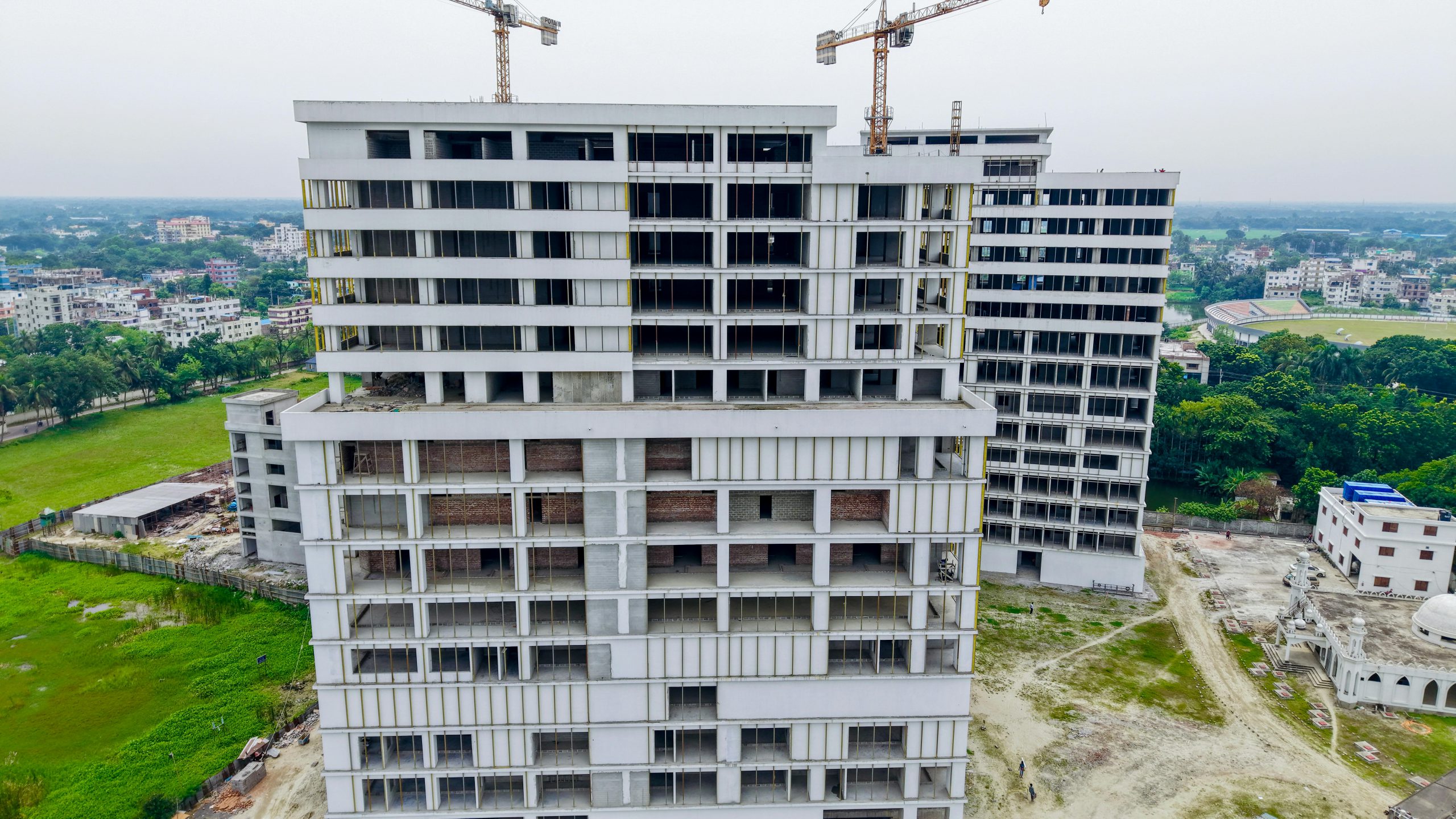 Aerial shot showcasing a high-rise building under construction with cranes against a cityscape backdrop.